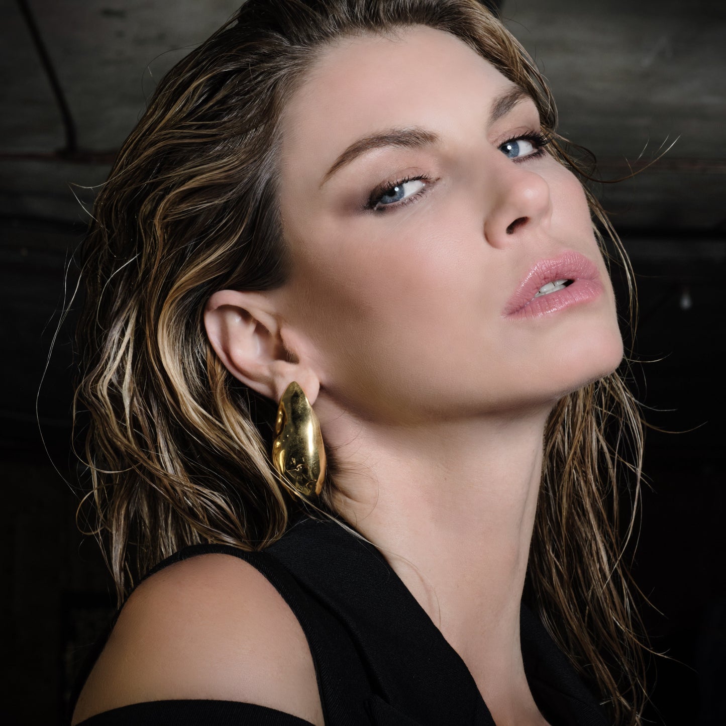 Glam beauty: Woman wearing gold earrings against a dark background